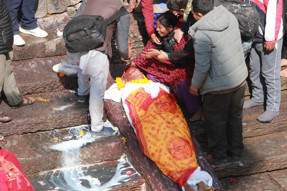 Der Leichnam wird zu der abschüssigen Stelle, die direkt in den Bagmati Fluss mündet, gebracht.  Oberhalb des Kopfes befindet sich ein Loch bzw. ein Durchbruch mit einer Quelle.  Daraus wird mit der hohlen Hand eine Flüssigkeit aus Wasser und Milch geschöpft und dem Toten in den Mund geträufelt. Der Körper ist in ein Tuch gewickelt. Neben dem nicht verhüllten Kopf sind brennende Räucherstäbchen in die Bodenritzen gesteckt. Der Leichnam ist in orangefarbene Tücher gewickelt.